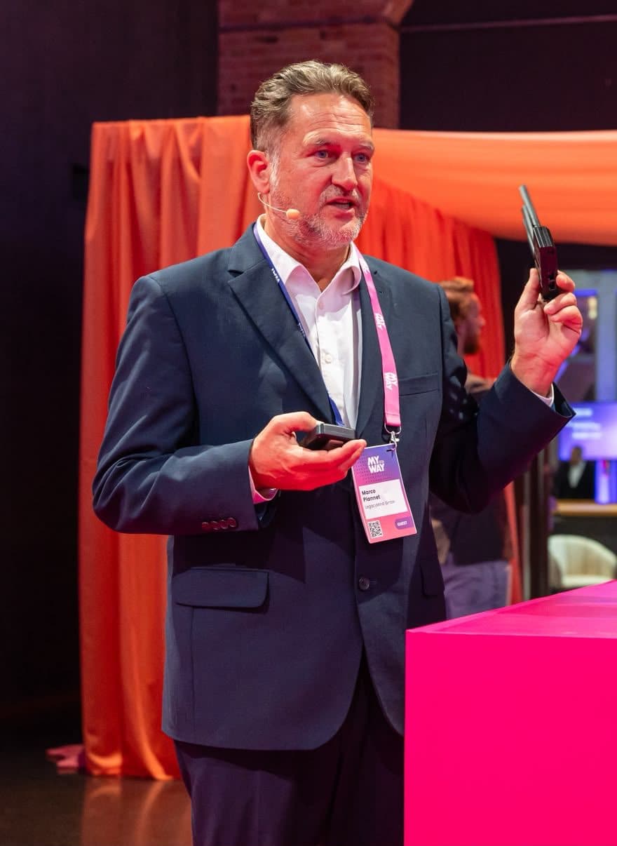 Marco Plannet auf der Bühne der MyWay 2026, den Router aus dem Vortrag in der erhobenen Hand